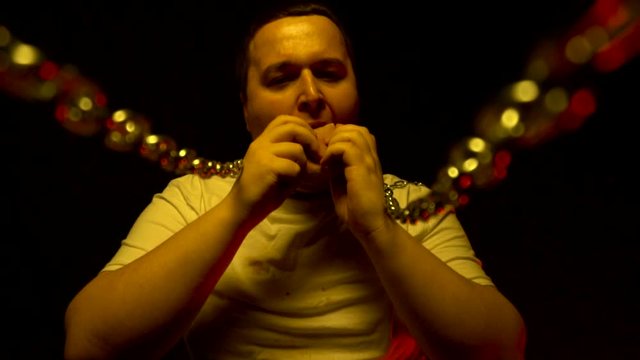 Fat man eating fast food whose chains are on his neck. Hostage concept of junk food and drink, slow motion
