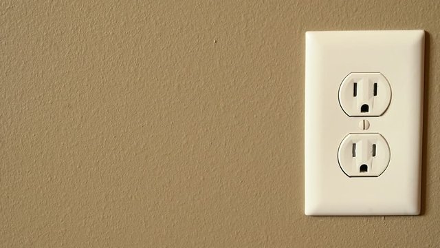 Front view of Caucasian hand gripping a three pronged power cord to remove it from a power outlet