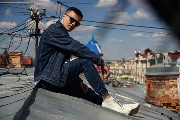 guy in a jeans suit and sunglasses sits on the roof