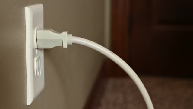 Caucasian hand gripping a three pronged power cord to plugin to a power outlet