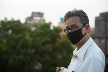 portrait of an Indian old man with corona preventive mask on a rooftop during sunset in home isolation.Indian lifestyle, disease and home quarantine.