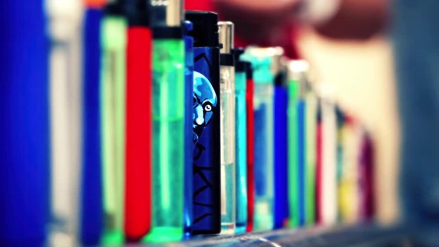 Cinemagraph of cartoon face of a man on blue lighter that looking at camera and blinking. He glances between many other lighters that are lined up. Closeup, loop, selective focus with copy space.