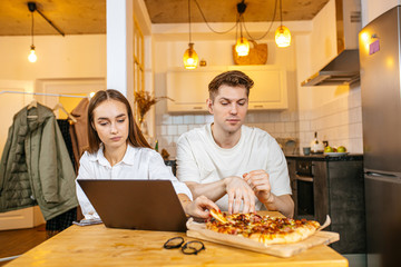 happy caucasian married couple eat pizza from delivery service and watch film in laptop. romantic husband ordered home delivery, he pleased his beloved with food