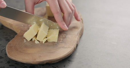 man hands cut cheddar cheese in cubes on olive wood board