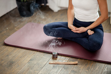 cropped photo of unrecognizable calm yogi female sit on the floor in lotus pose, meditate at home during quarantine, every morning begins from yoga, she use incense sticks