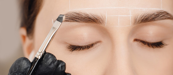 Correction and tinting eyebrows, master applies brush to woman marking on brow. Cosmetic procedures...