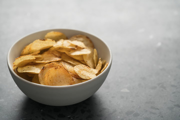Potato chip slightly sprinkled with black pepper in white bowl on concrete background with copy space