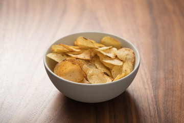 Potato chip slightly sprinkled with black pepper in white bowl on walnut wood background with copy space