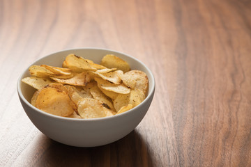 Potato chip slightly sprinkled with black pepper in white bowl on walnut wood background with copy space