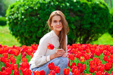 Young beautiful girl in a summer dress posing on the lawn with red tulips