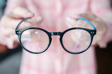 Glasses in blue rims in female hands on a background of a pink plaid shirt.