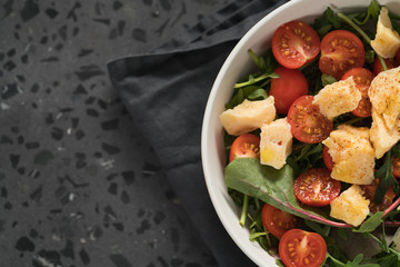 salad with cherry tomatoes, mixed grens and cheese in white bowl on concrete background