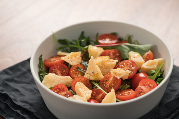 salad with cherry tomatoes, mixed grens and cheese in white bowl on wood table