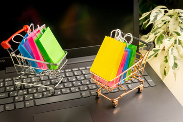 online shopping concept. little shopping cart with colorful shopping bags inside  stand near...
