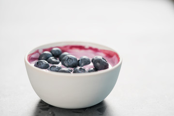 Blueberry yogurt with whole berries in white bowl on concrete background