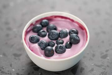 Blueberry yogurt with whole berries in white bowl on concrete background