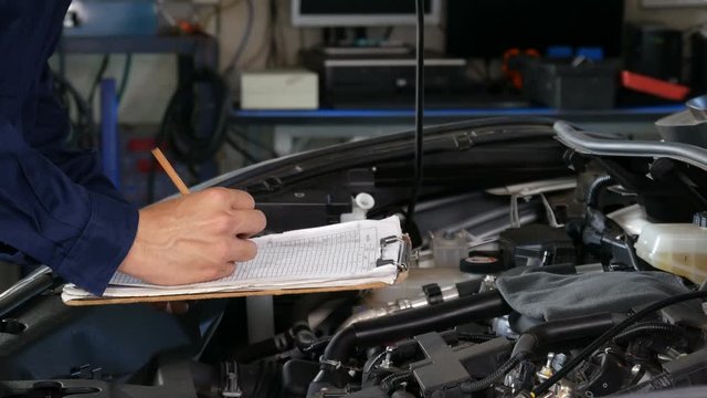 male mechanic checking and repair service a car with clipboard