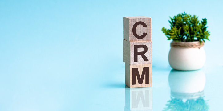 Cube wooden block with alphabet combine the word abbreviation CRM on blue background.