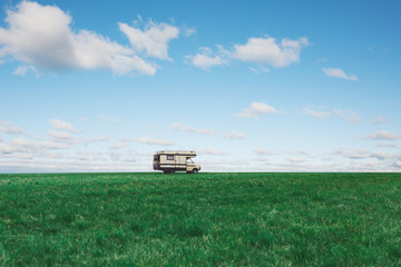 Fototapeta premium Camper van in the green field on background of blue sky with clouds. Motorhome on nature. Travelling