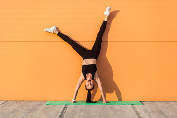 Overjoyed excited girl with perfect athletic body in tight sportswear doing yoga handstand pose...