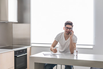 Man using his cell phone while working on finances in his home kitchen.