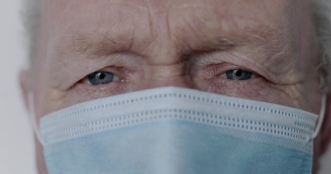 Close view into camera of senior man with medical mask, lowers crestfallen eyes