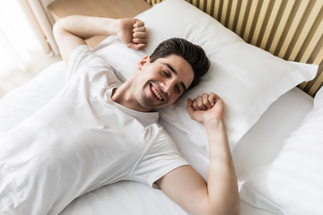 Young handsome happy man waking up on bed, top view