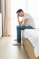 Worried or depressed man sitting on bed with hand on forehead