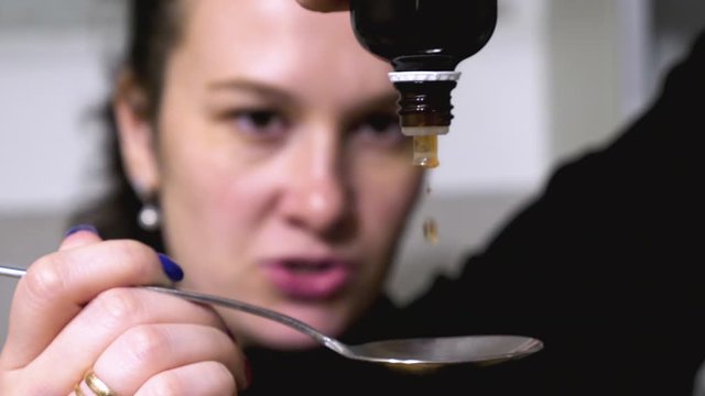 female hands pouring medicine drops onto tablespoon at home