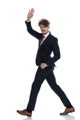 Side view of positive businessman waving with hand in pocket