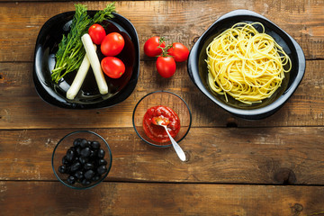 Black plate with pasta and vegetables to decorate Italian dishes on a wooden table.