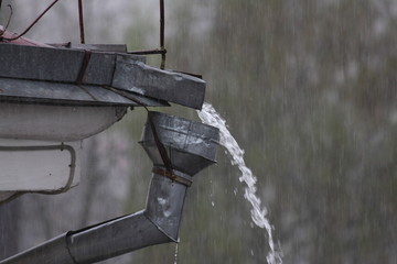 Rainwater stream from the roof overflows through the funnel of the drainage pipe closeup, a heavy...