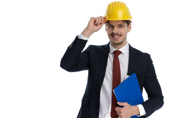 Happy businessman holding clipboard while fixing his construction helmet