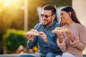 Picture of happy young couple eating pizza outdoors