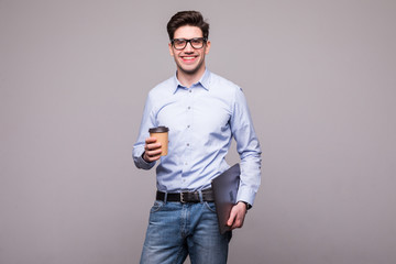 Portrait of handsome young man dressed in shirt holding takeaway coffee and laptop and looking away...