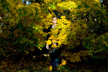 Introverted woman is standing among vibrant yellow and green maple foliage looking sad, thoughtful,...