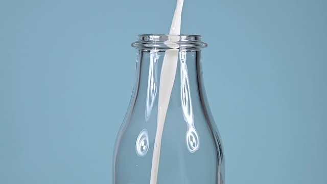Close up pouring milk in glass bottle over blue