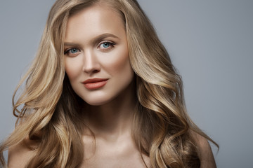 Fototapeta premium Beautiful confident blonde woman with blue eyes, luxury wavy hair, natural colors makeup. Close up beauty studio portrait. Copy, empty space for text