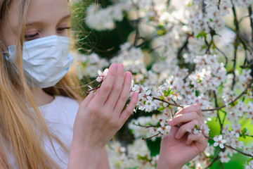 Teenager girl in medical mask in spring flowering garden. Concept of social distance and prevention of coronavirus.