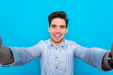 Handsome young man is making selfie and smiling on blue background