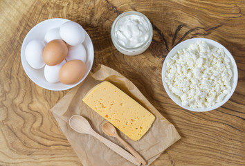Rustic products on a textured wooden table: cottage cheese, eggs, sour cream and cheese. Healthy food, a source of useful natural calcium and vitamin D