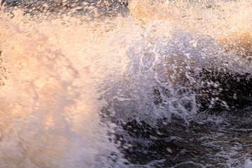 Waves break on a stony beach and form a large spray with sunset colors