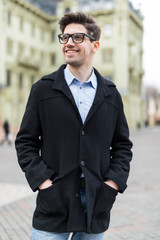 Young man with a smartphone in his hand, walking in the street. Young guy with modern hairstyle in urban background.