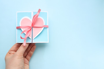 A small blue holiday card with a pink heart and a ribbon in the hand of a Caucasian man on a blue background. Space for text.Selective focus. Valentine's day and Mother's day greeting cards.copy space