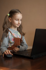 Serious little girl is concentrated in front of her black laptop while focused on doing homework during the quarantine because of the pandemia of Coronavirus Covid-19. Remote education