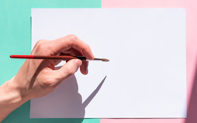 The man is holding a paint brush with his left hand and is about to write on a pad of paper....