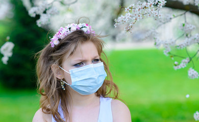 Teenager girl in medical mask in spring flowering garden. Concept of social distance and prevention of coronavirus.