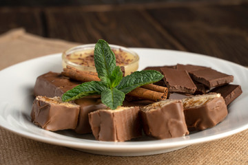 Plate with sweets: chocolate, sweets, honey, cinnamon and mint on a natural background. The concept of relaxation, eating.