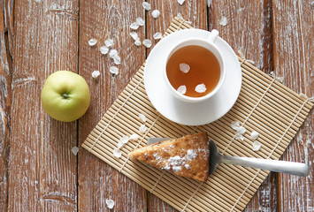 Homemade apple pie with cinnamon and cup of tea on wooden table.