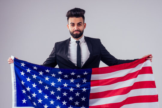 arabian young handsome black hair man in stylish business suit holding american flag in studio isolate white background.Independence Day concept